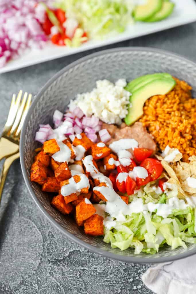 the sweet potatoes in the taco bowl covered in a sour cream sauce. Two gold forks off to the left of the bowl.