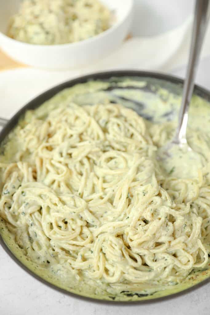 the basil alfredo sauce in the pan with a large silver spoon.