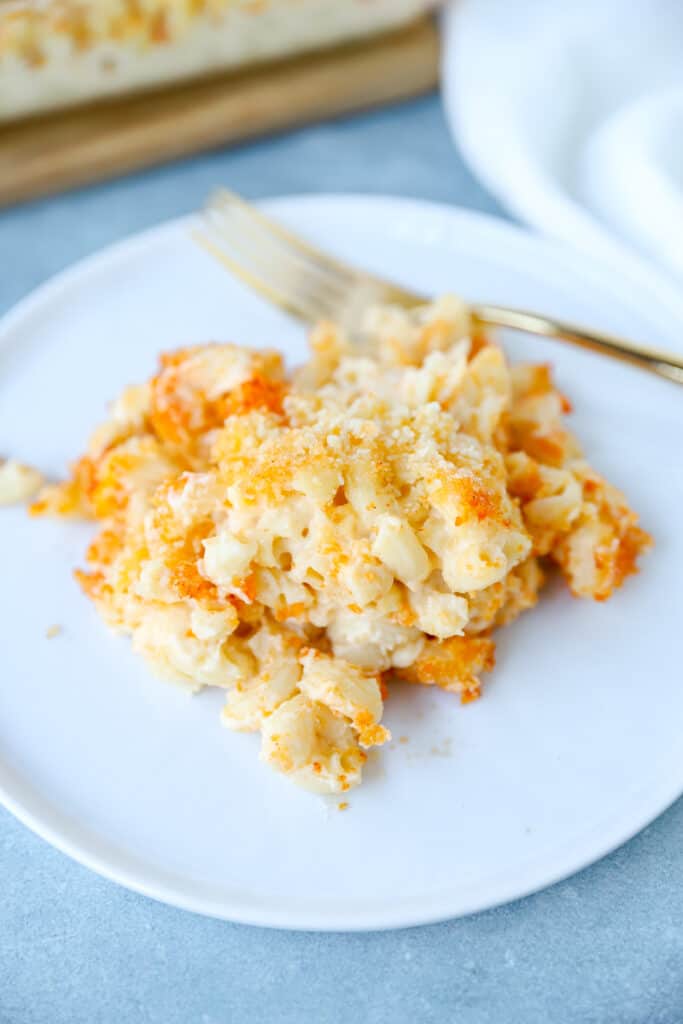 the baked mac and cheese serving on a round white plate on a light blue surface.