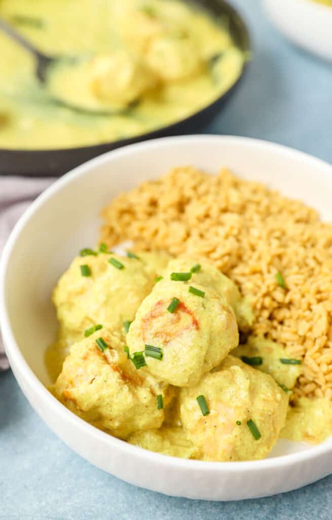 creamy curry sauce chicken meatballs in a white bowl topped with diced chives