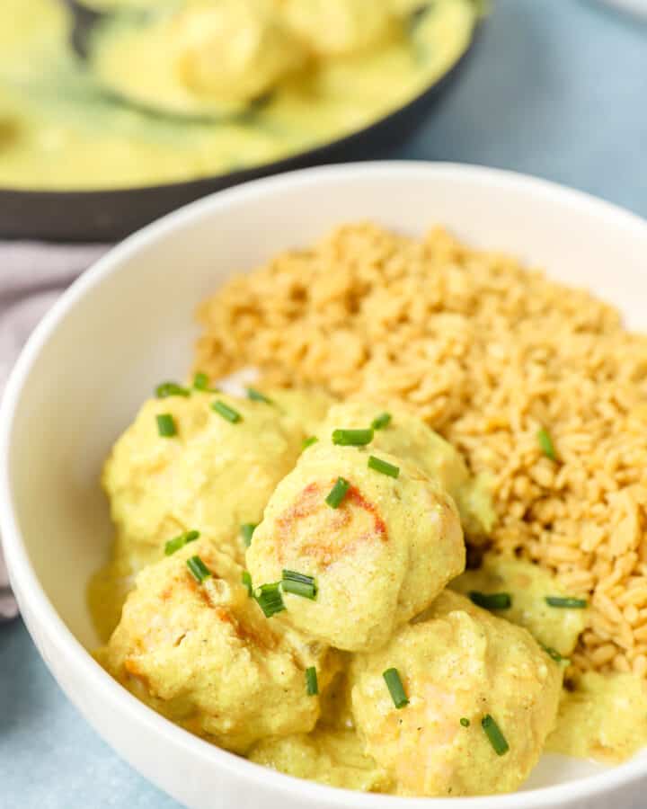 creamy curry sauce chicken meatballs in a white bowl topped with diced chives