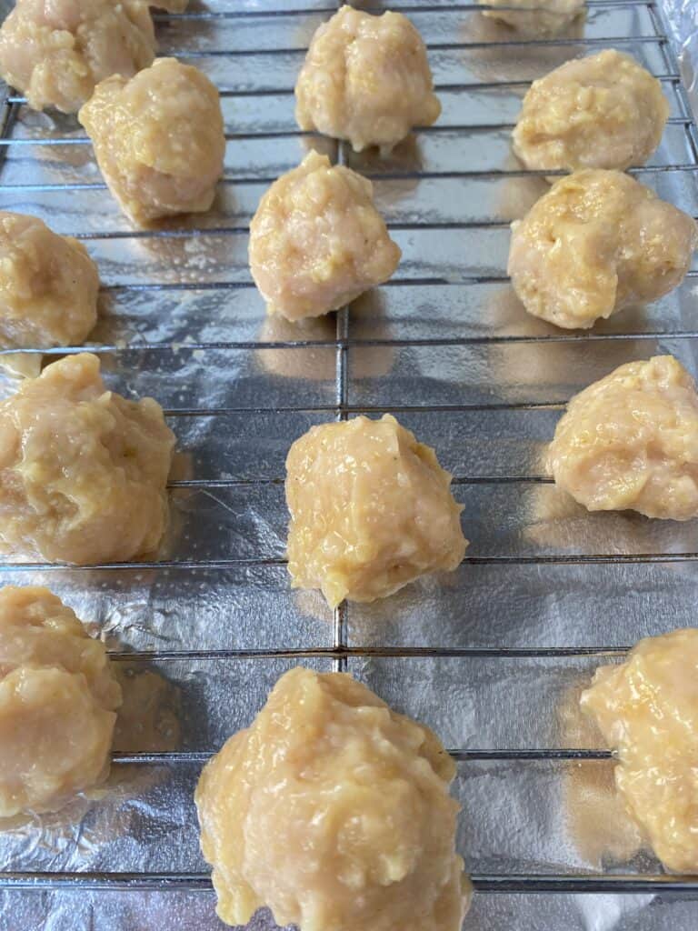 the raw meatballs on a baking rack on a foil lined sheet pan.