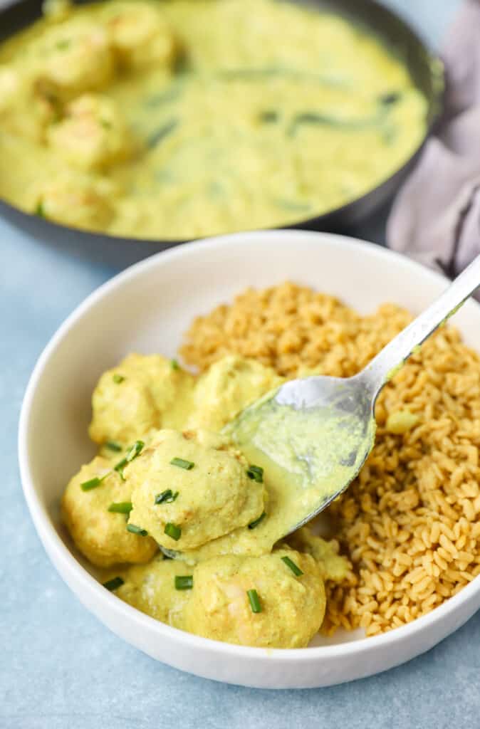 creamy curry sauce chicken meatballs being spooned into in a white bowl topped with diced chives