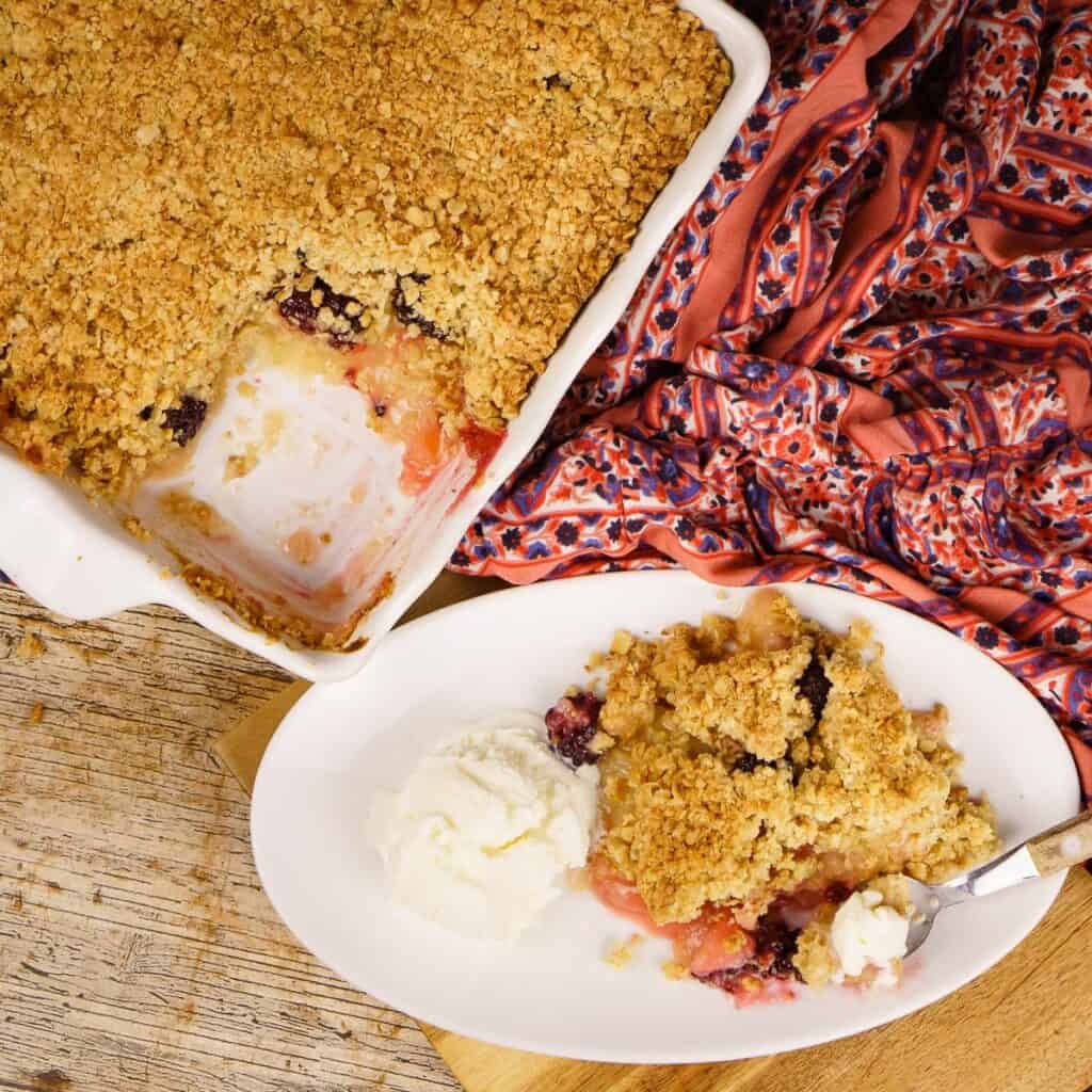 overhead photo of the apple blackberry crumble in a white casserole dish with a slice removed.
