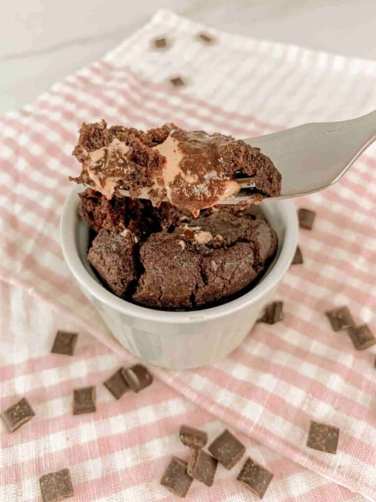 the mug cake on a red checkered linen with a fork full of the mug cake showing the interior texture.