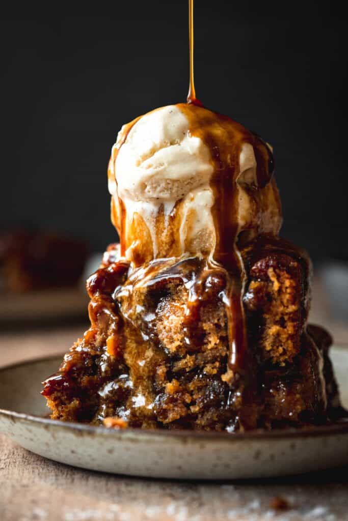 ice cream topped sticky toffee pudding with toffee sauce being drizzled over top.