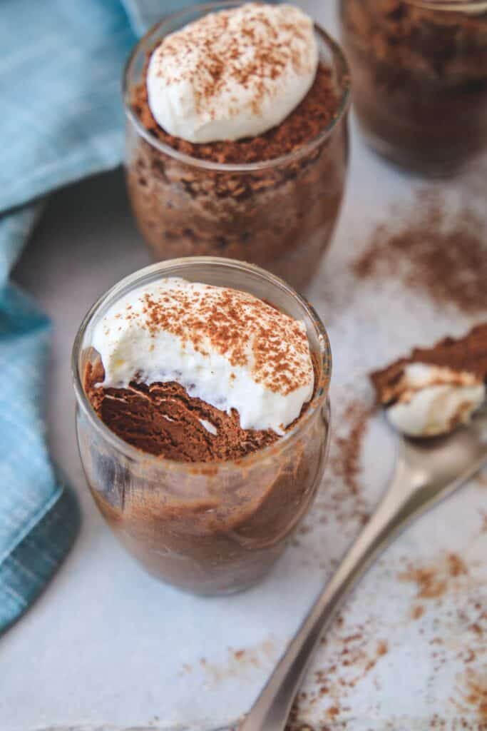 the chocolate mousse in a glass jar with a scoop removed, the spoon with the mousse is below the jar slightly blurred.