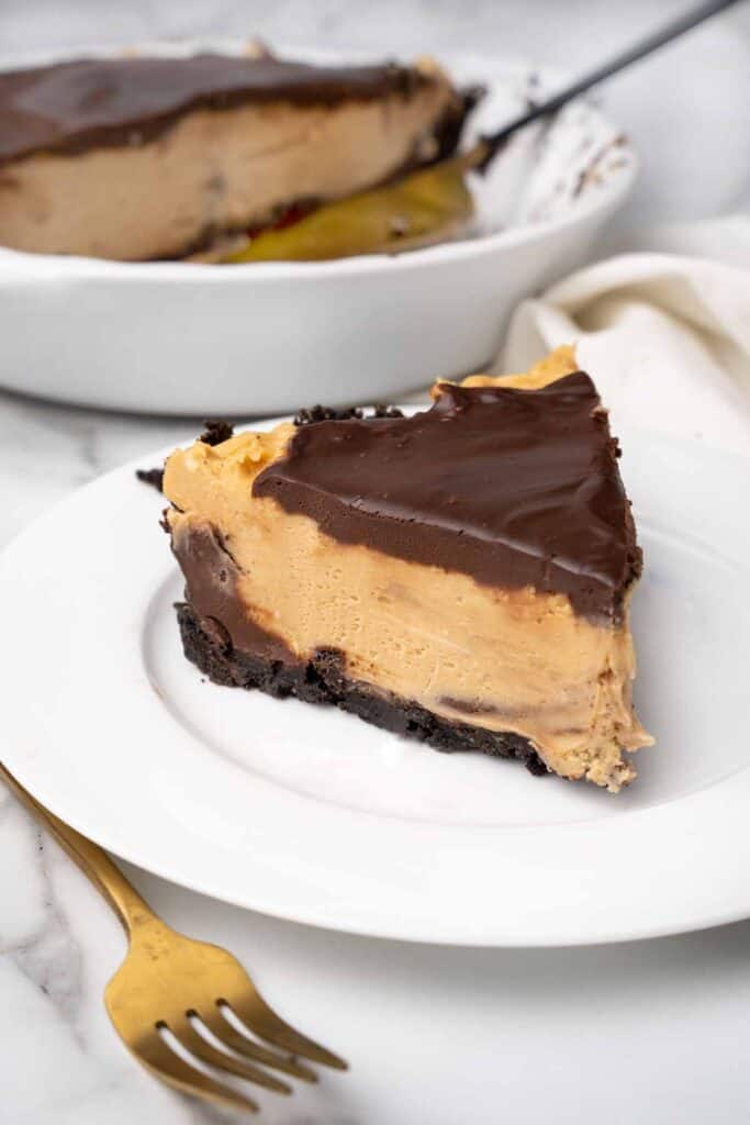 a round white plate with a slice of chocolate peanut butter pie, the pie plate in the background.