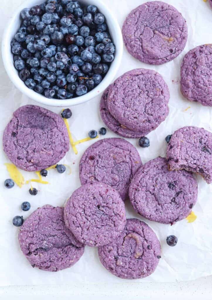 overhead photo of the blueberry lemon cookies with a bowl of blueberries and lemon peel and fresh blueberries scattered about.