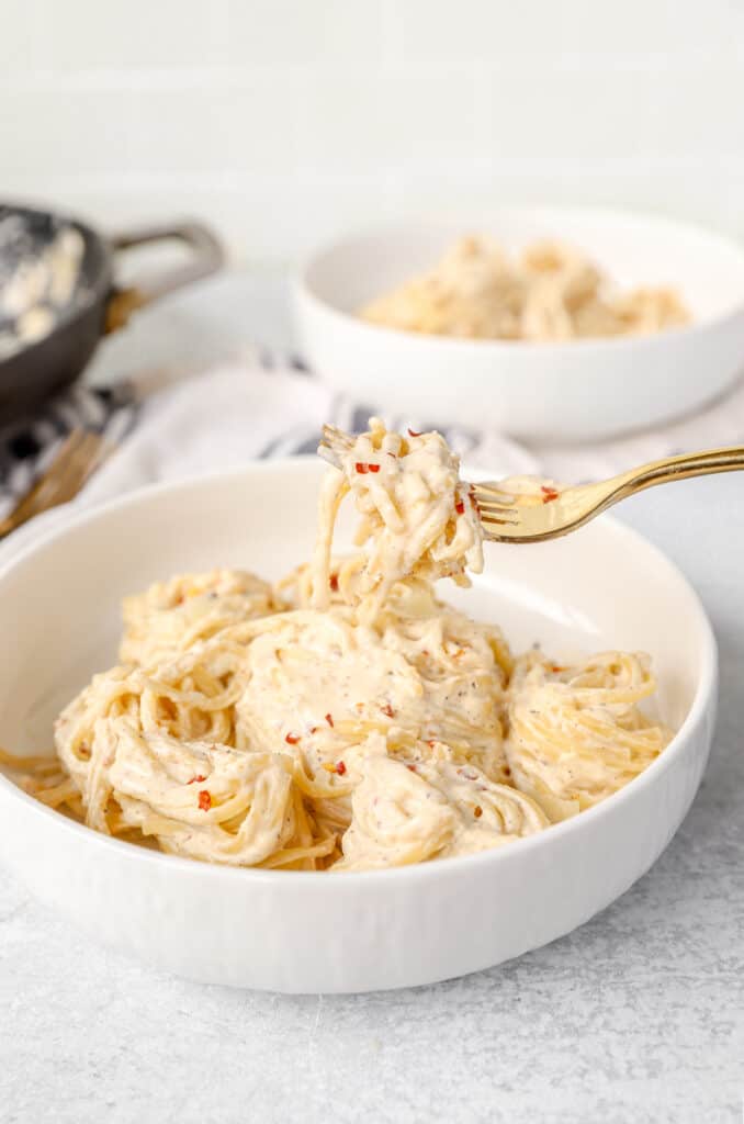 a gold fork scooping the spicy Alfredo from the white bowl.