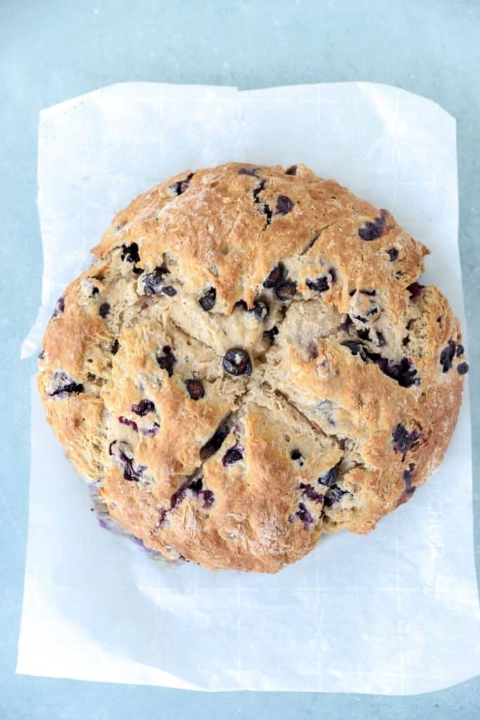 overhead photo of the baked blueberry soda bread load on a piece of parchment paper on a blue surface.