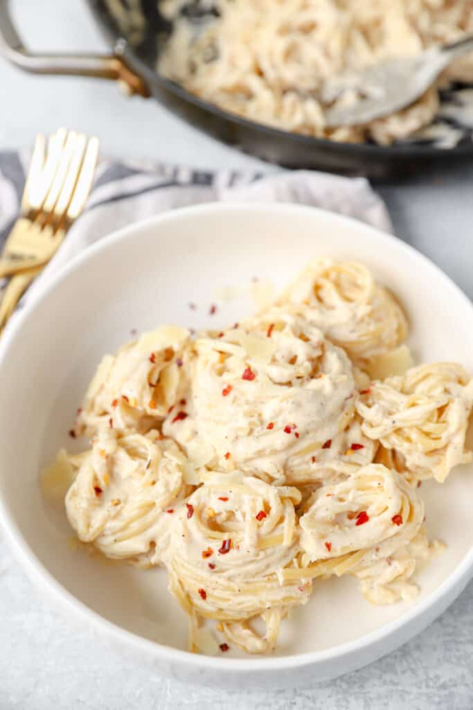 the spiraled spicy Alfredo sauce noodles garnished with more red pepper flakes in a white bowl.