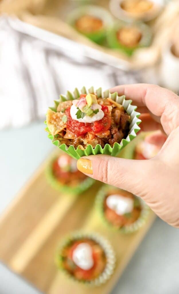 a hand holding a walking taco casserole in a green muffin liner