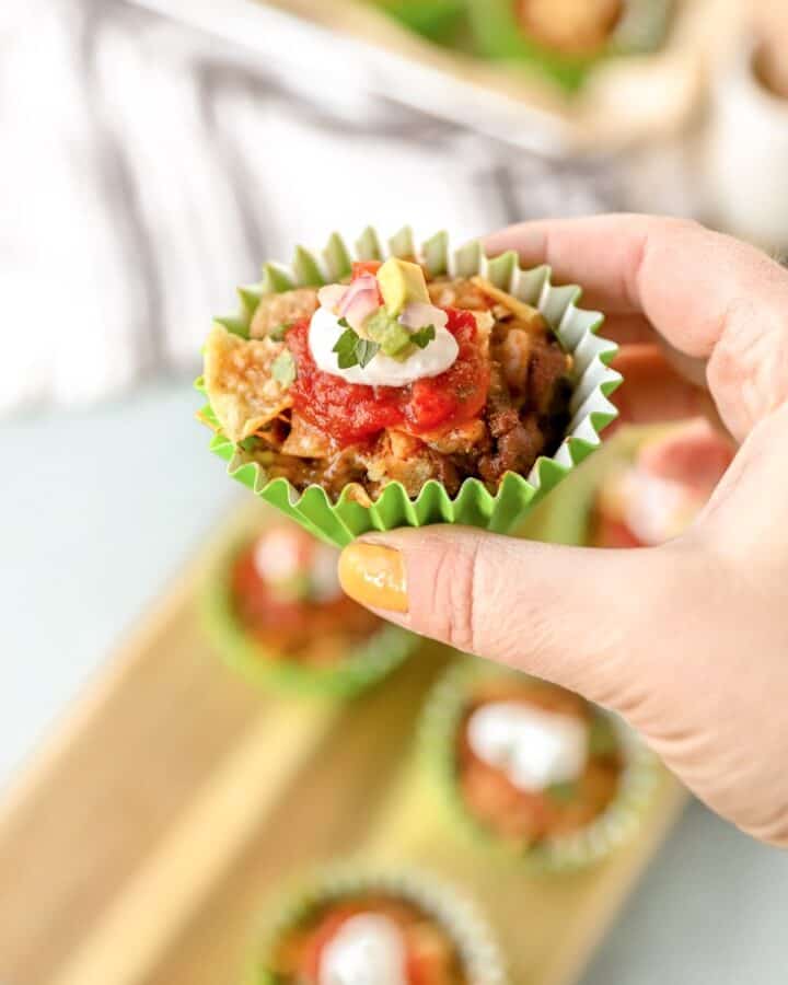 a hand holding a walking taco casserole in a green muffin liner