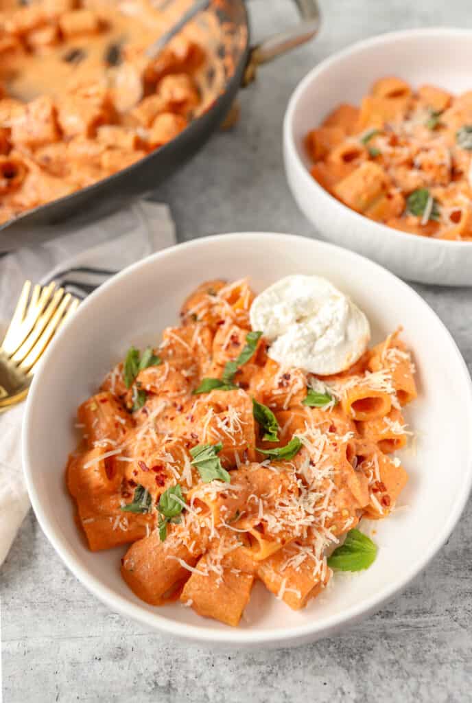 spicy vodka sauce pasta in a round white bowl with Burrata and fresh chopped basil.