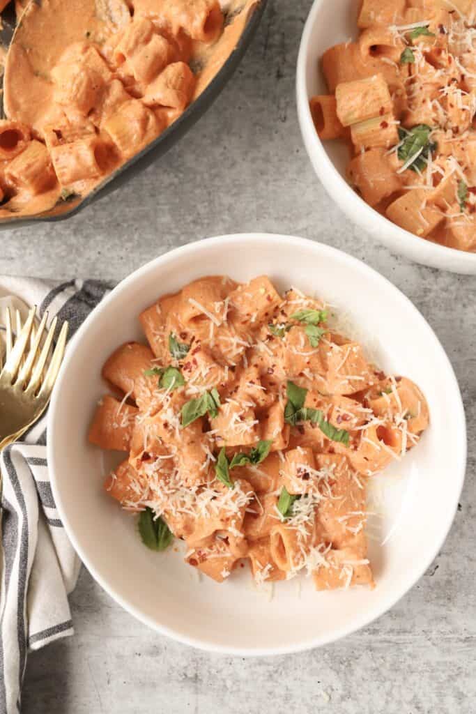 overhead photo of the pasta in a white round bowl with two gold forks to the left on a navy and ivory striped linen napkin.