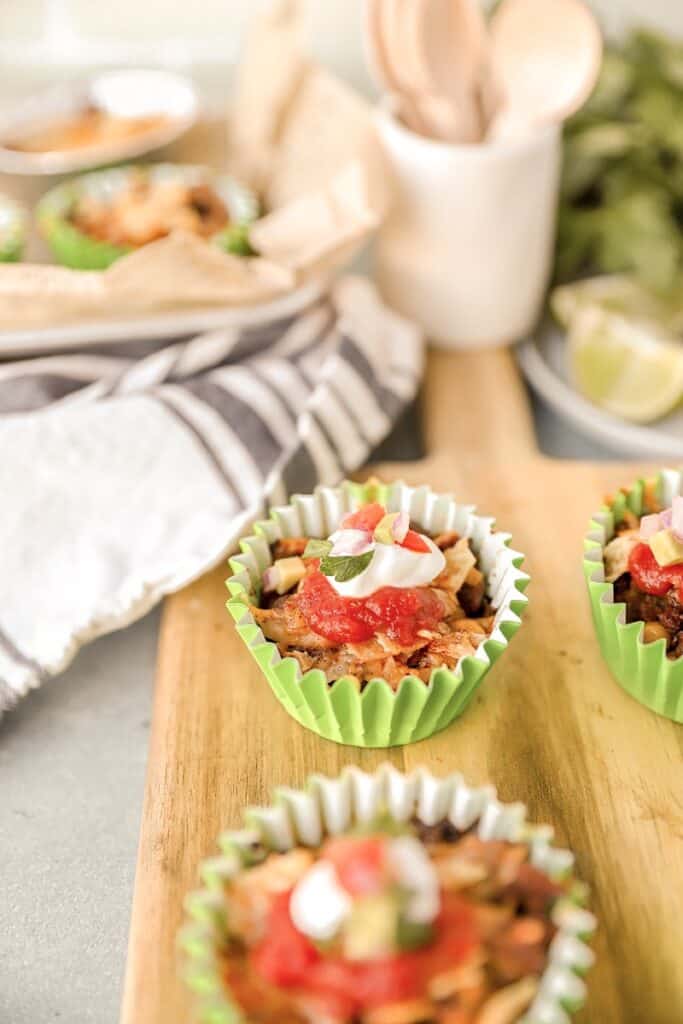 walking taco casserole in a green muffin liner on a wood cutting board.