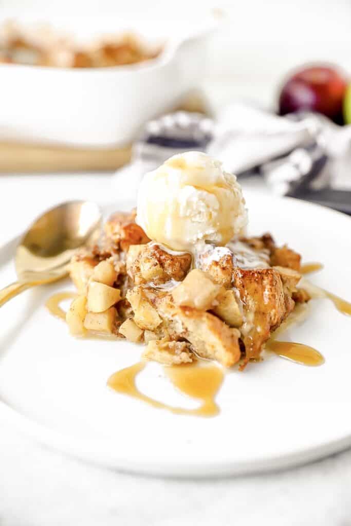 apple biscuit bread pudding on a white plate with ice cream on top.