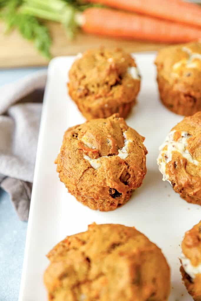 pumpkin carrot cake muffins on a white platter with carrots in the background.