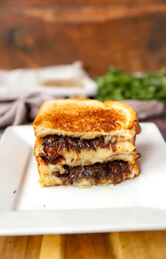 two slices of the French onion grilled cheese stacked on a white plate.