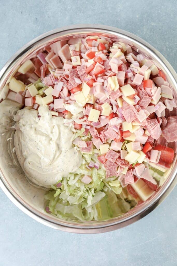 overhead photo of all the grinder salad ingredients with the dressing before mixing it in a silver bowl.