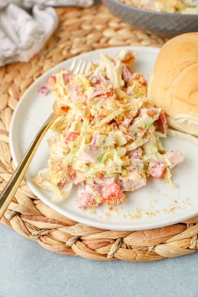 the grinder salad on a white plate with a gold fork and a dinner roll. The plate is on a brown rattan place mat.