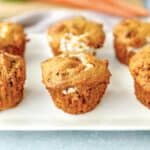 pumpkin carrot cake muffins on a white platter with carrots in the background.