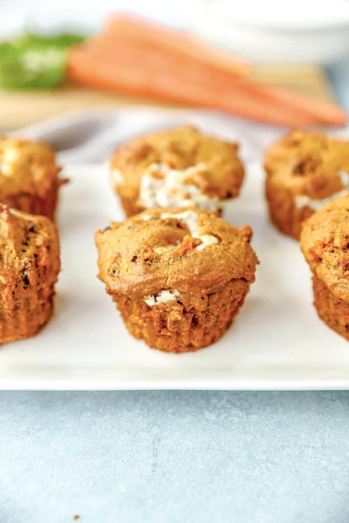 pumpkin carrot cake muffins on a white platter with carrots in the background.