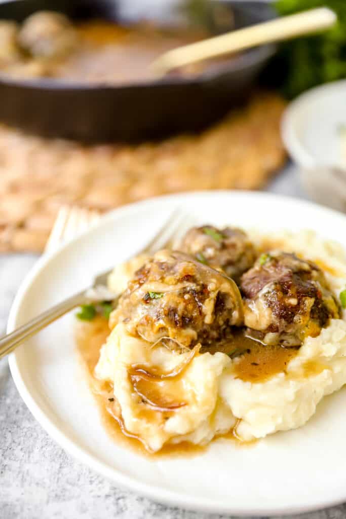 meatballs in mashed potatoes on a white plate with a gold fork