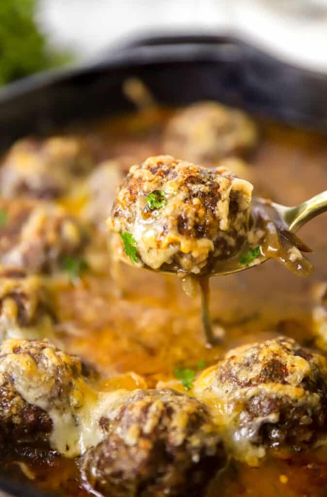 scooping one of the meatballs from the skillet.