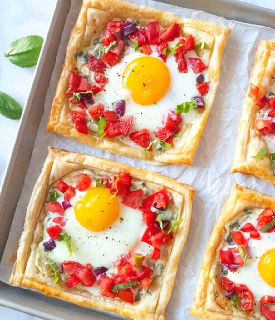 egg and tomato tarts in puff pastry on a baking sheet.