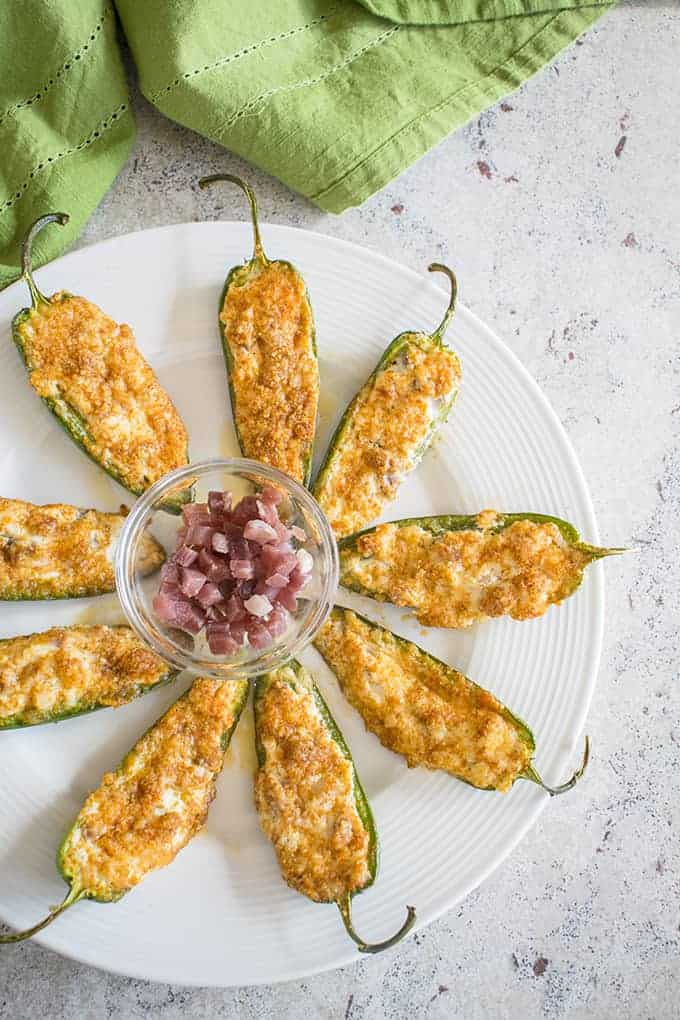 Baked jalpeno poppers  on a round white plate with prosciutto