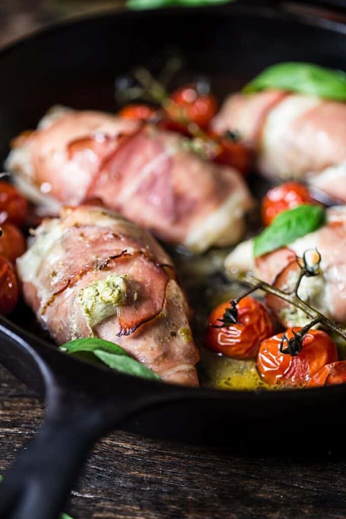 chicken breasts wrapped in prosciutto with tomatoes in a cast iron skillet