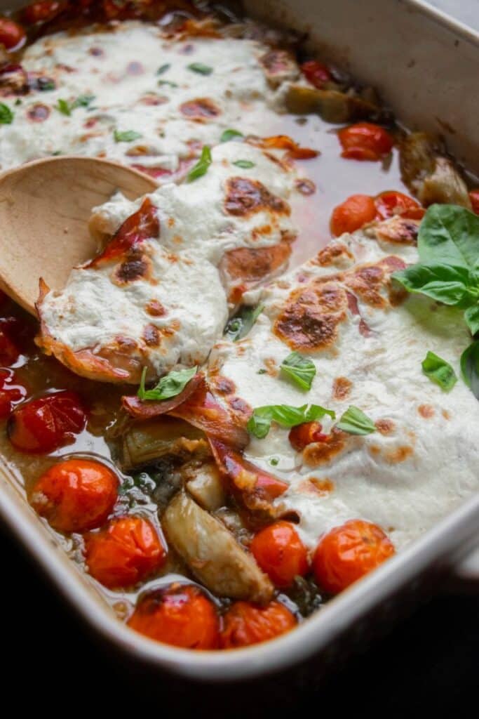 mozzarella prosciutto chicken in a casserole dish with a wooden spoon.