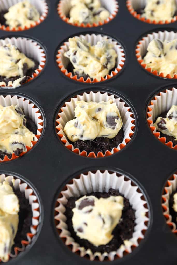 the unbaked muffins in the pan now topped with the orange cream cheese filling.