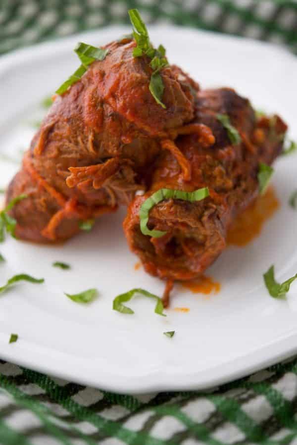 two beef bracioles on a white plate topped with basil