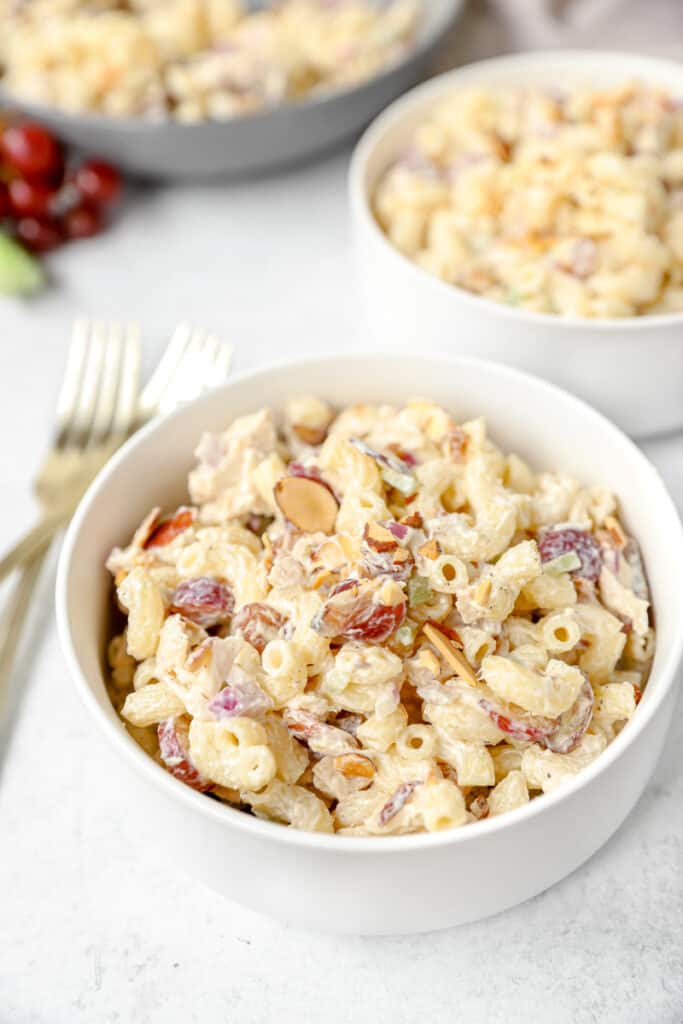 two white bowls with the pasta salad and two gold forks.