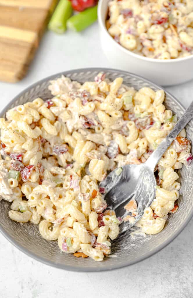 the pasta salad in a grey round bowl with some removed and a large silver spoon scooping.