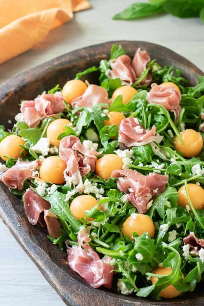 melon arugula prosciutto salad in a wood bowl