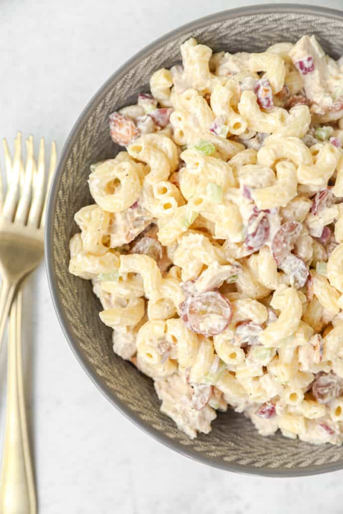 overhead photo of the chicken salad pasta salad in a grey bowl with two gold forks.