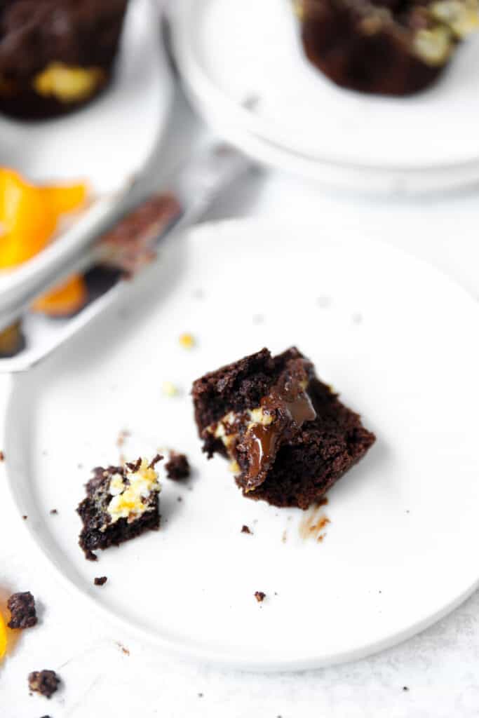 a piece of the muffin showing the melty chocolate interior on a round white plate.