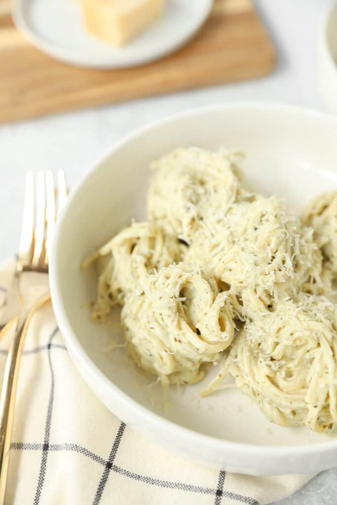 swirls of pesto alfredo pasta in a white bowl with a gold fork