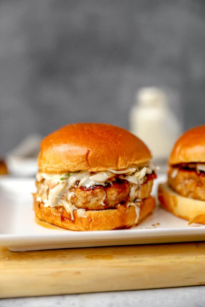 chicken teriyaki burgers on a rectangle white plate with a jar of ranch dressing in the background.