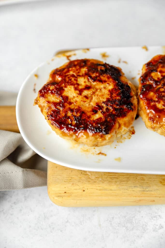 the cooked chicken burger on a white plate and on a wood cutting board.