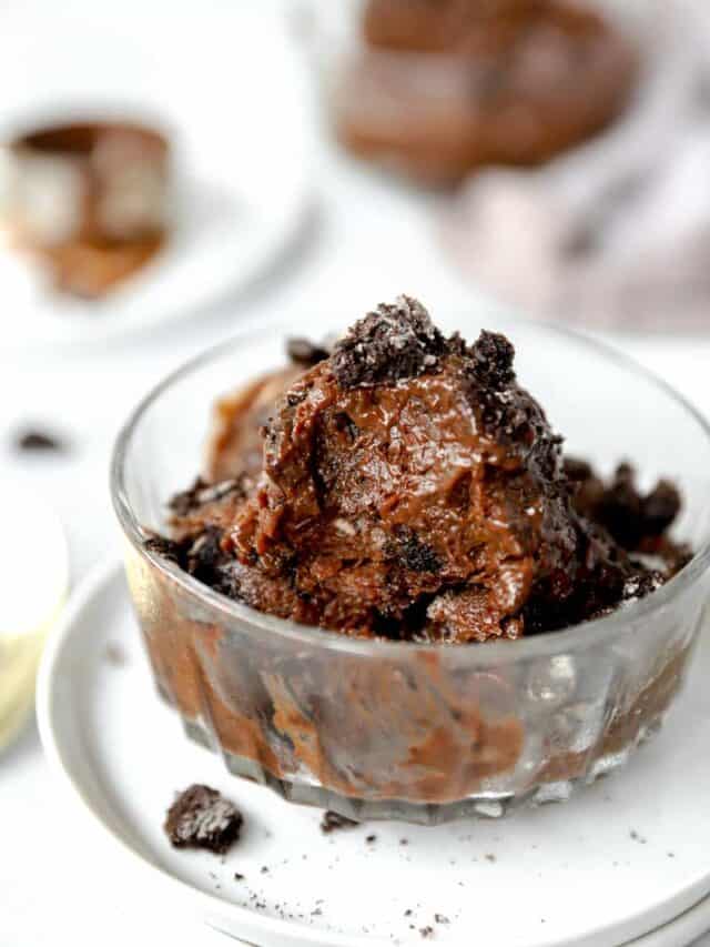 chocolate frozen pudding topped with crushed Oreo cookies on a glass bowl on a white plate.