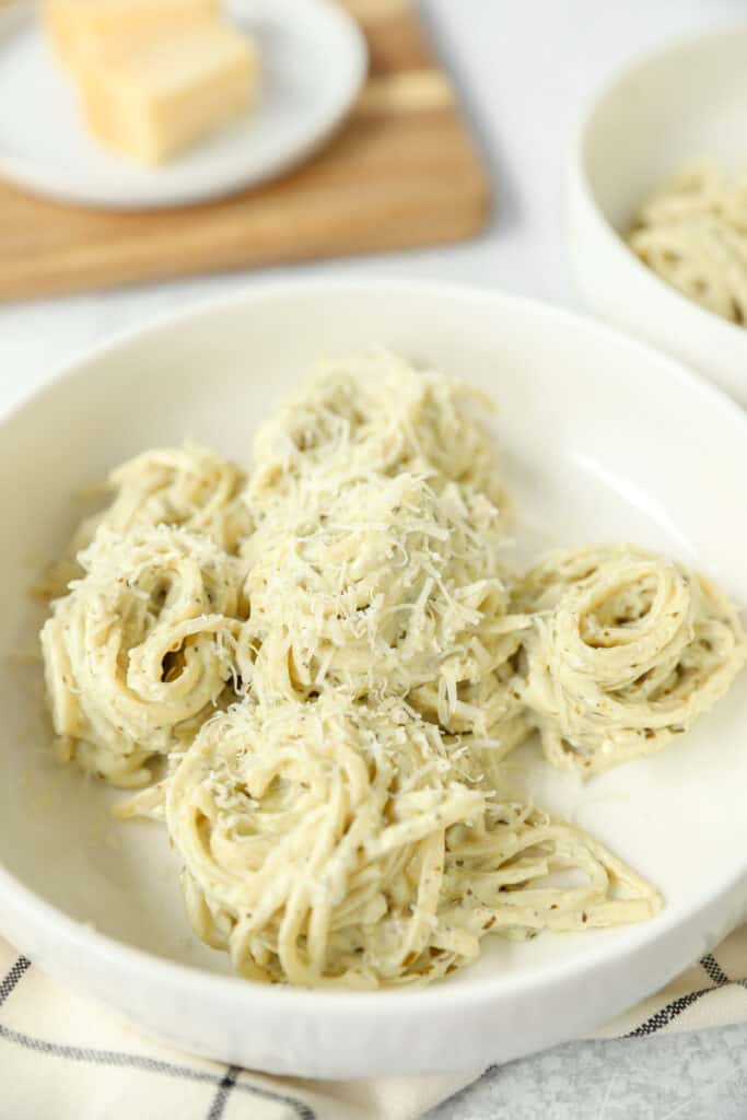 swirls of pesto alfredo pasta topped with grated Parmesan cheese in a white bowl.