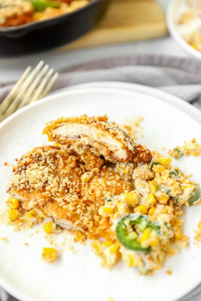 the chicken and corn and pepper mixture on a round white plate. The chicken thigh has been cut in half to show the interior texture of the meat.