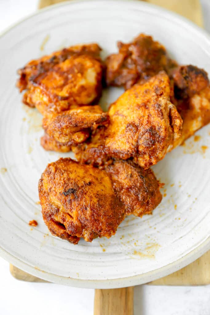 seasoned cooked chicken thighs on a grey round plate on a wood cutting board.