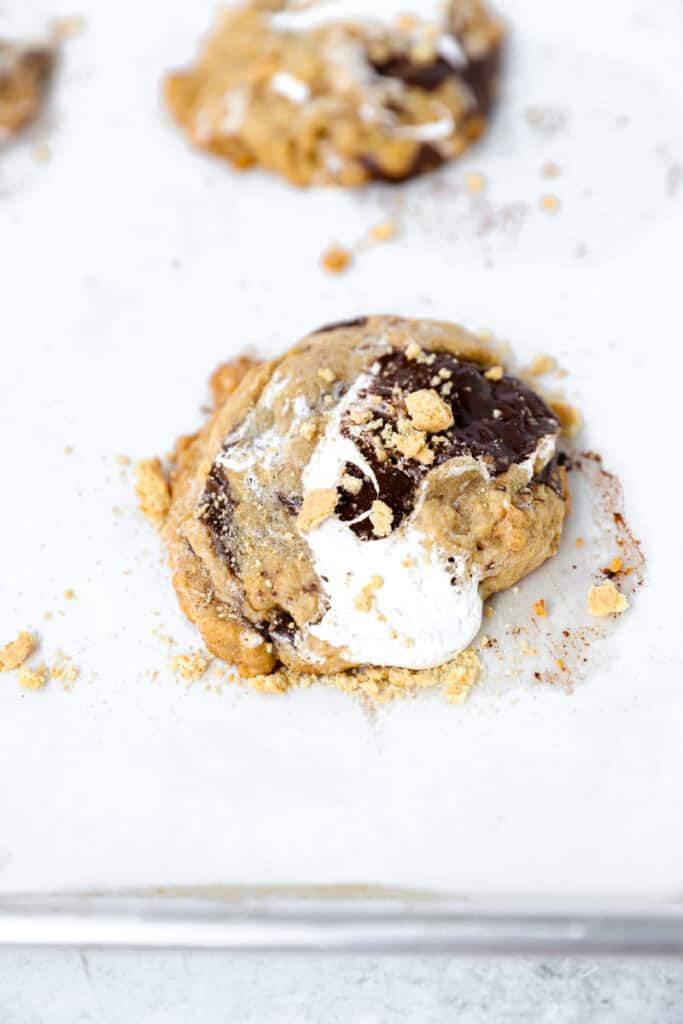 s'mores cookies topped with graham cracker crumbs on a parchment paper lined baking sheet