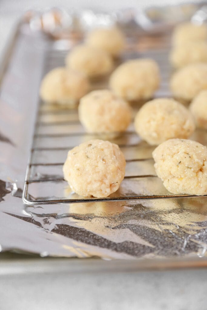 unbaked chicken meatballs on the baking rack on a foil lined baking sheet.